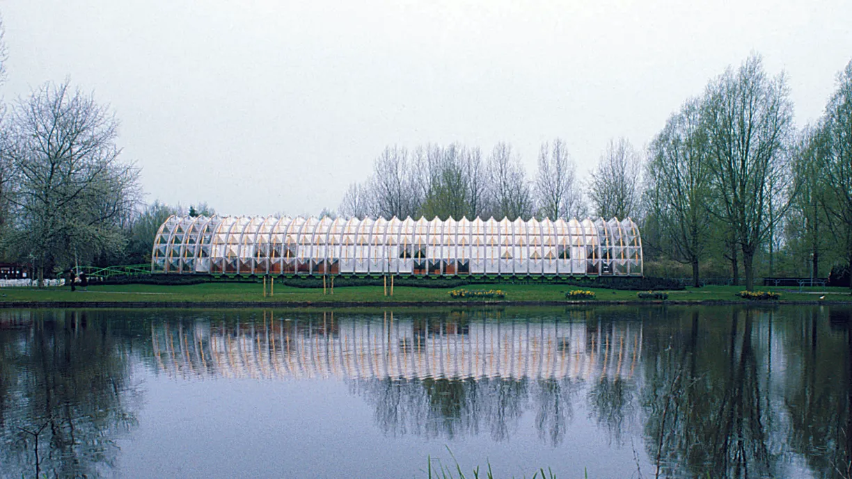 a greenhouse is sitting next to a lake in a park .