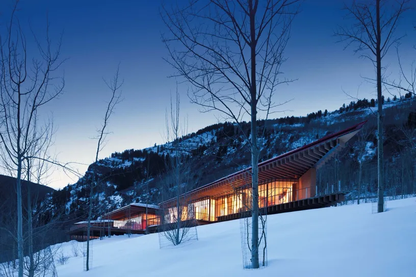 A large house is sitting on top of a snow covered hill