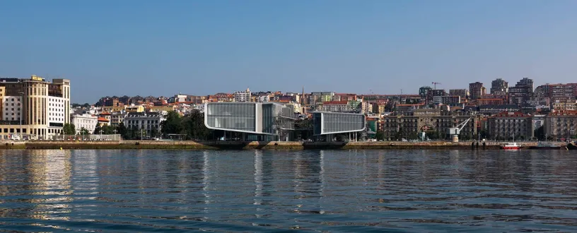A large building is sitting next to a body of water with a city in the background