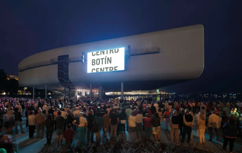 a large group of people are standing in front of a large building at night .