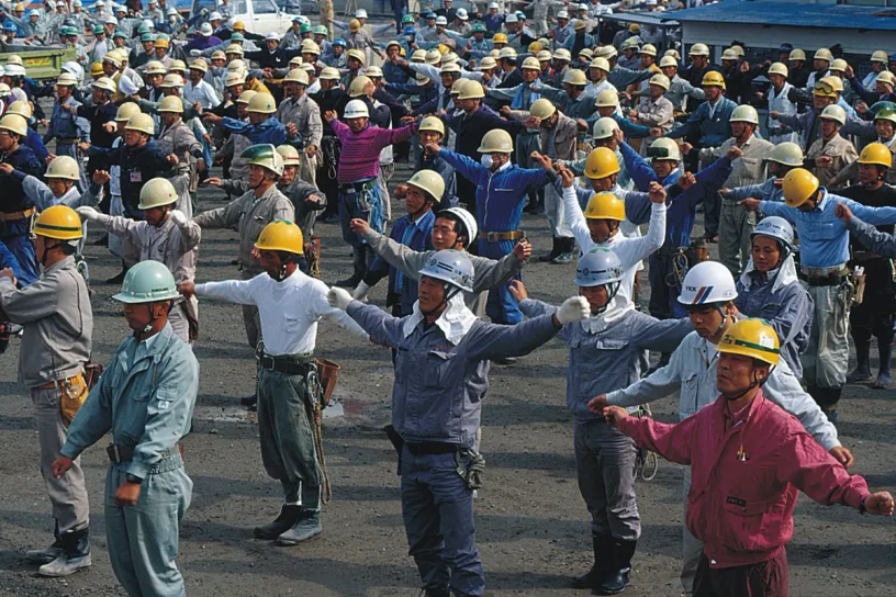 A large group of construction workers are doing stretching exercises
