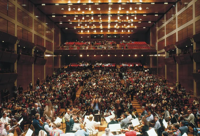A large group of people are playing instruments in a large auditorium