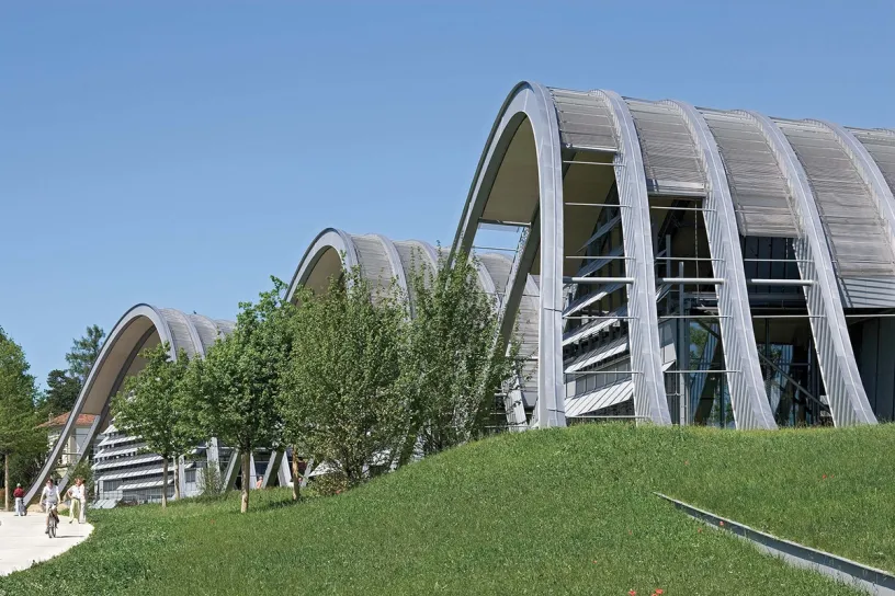 A large building with a curved roof is surrounded by grass and trees