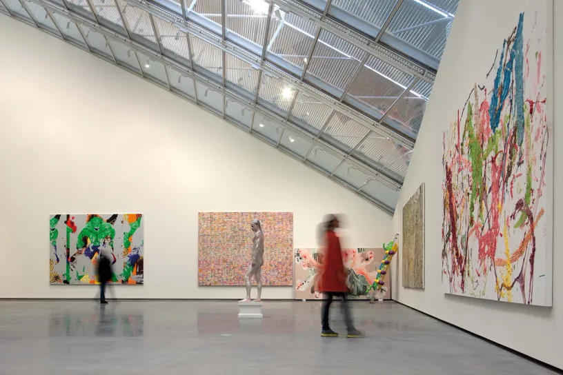 A group of people are walking through a museum with paintings on the walls