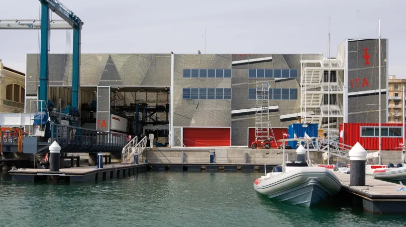 two boats are docked in front of a large building in a harbor .