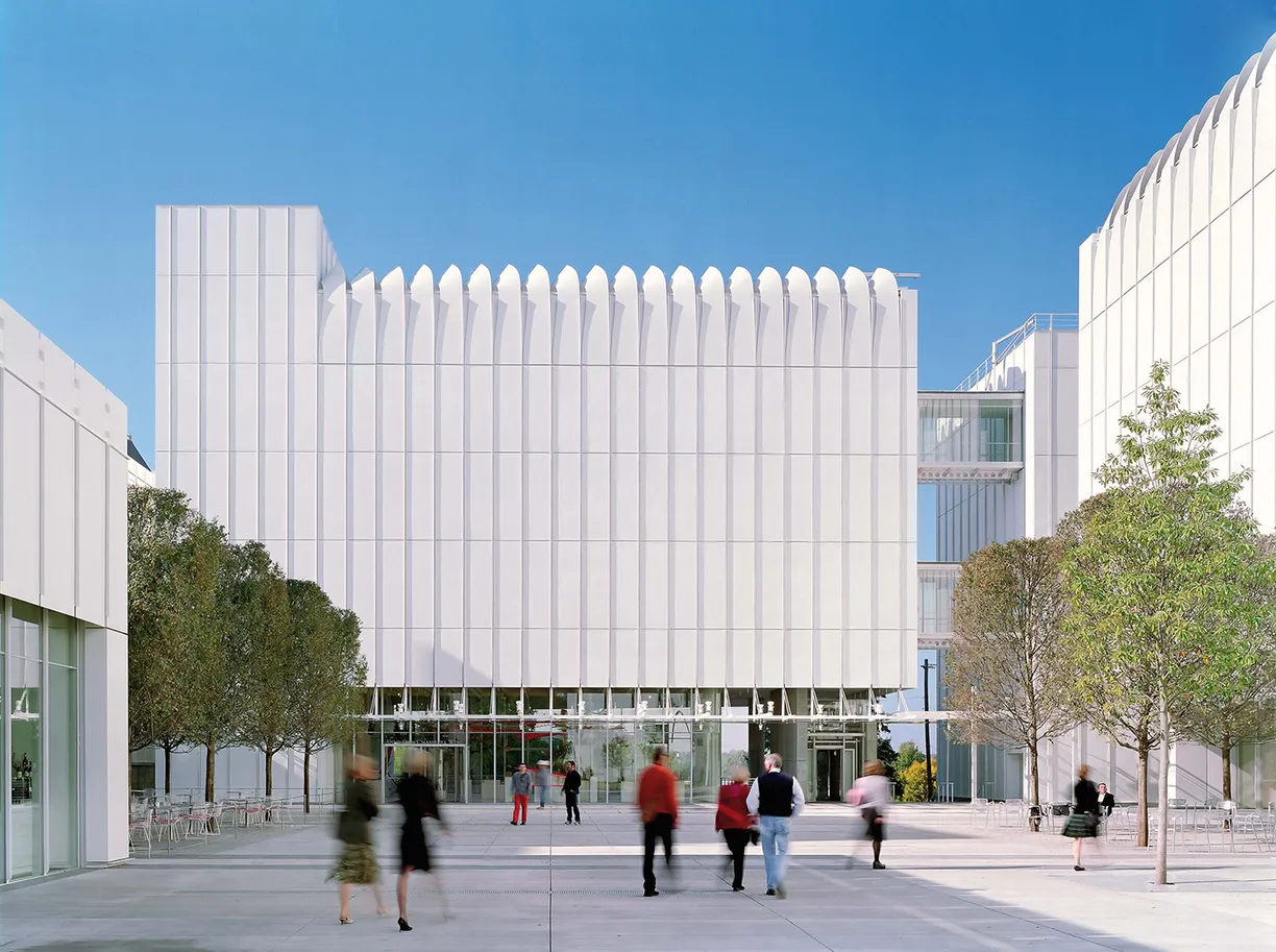 A group of people are walking in front of a large white building