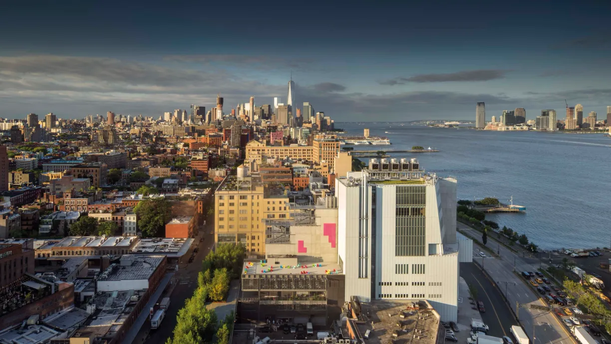 an aerial view of a city with a large building in the foreground and a large body of water in the background .