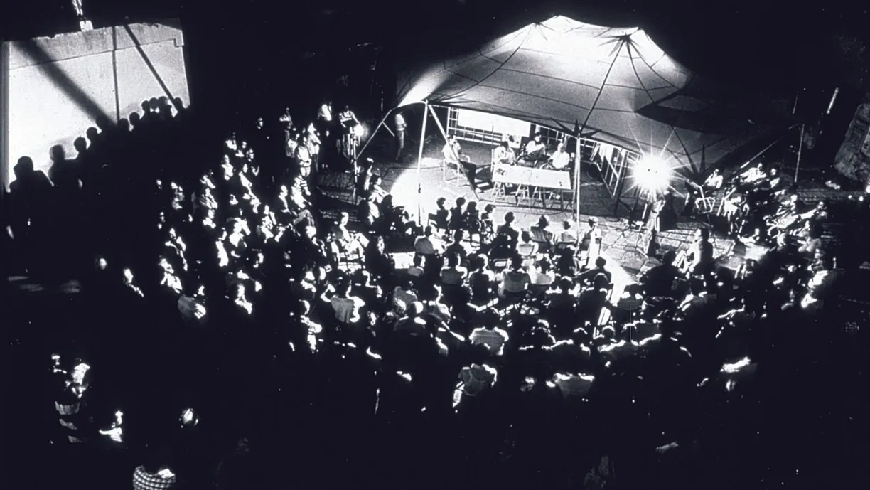 a black and white photo of a crowd of people watching a concert under a tent .