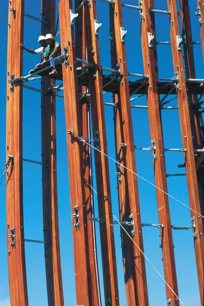 Two men are working on a wooden structure with a blue sky in the background