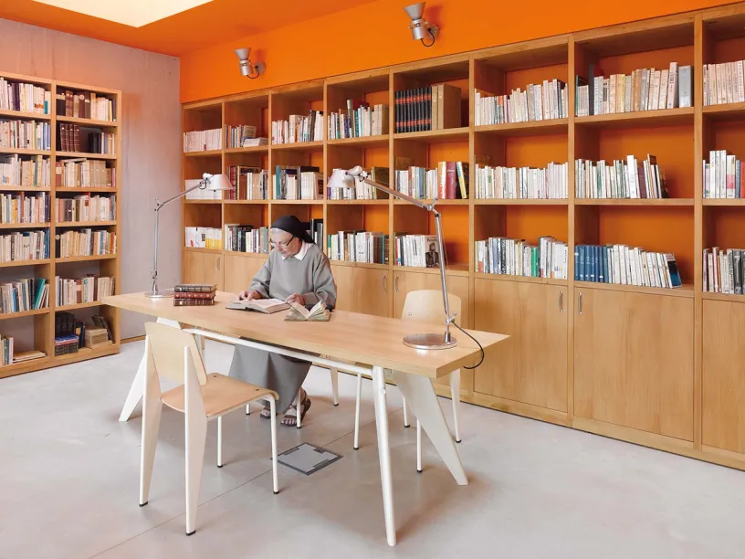 A monk is sitting at a table in a library reading a book