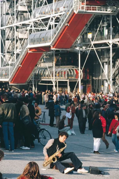 A man playing a saxophone in front of a large building