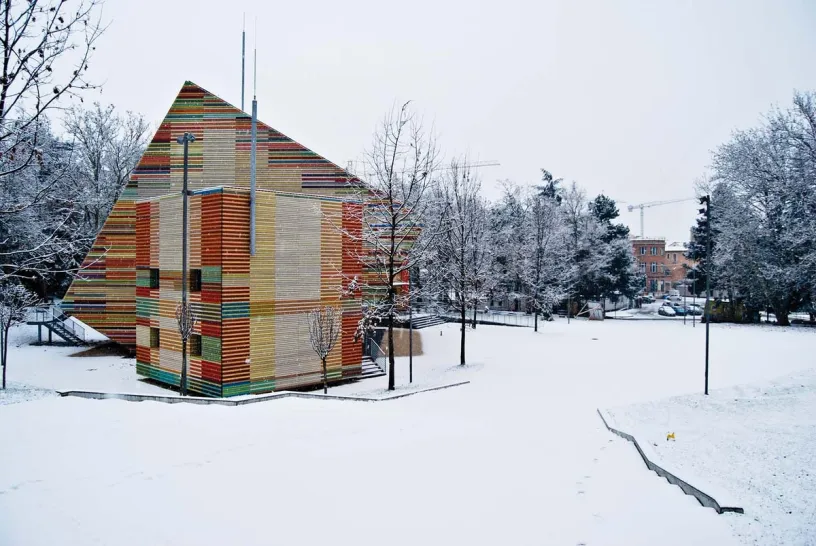 a colorful building is surrounded by snow and trees in a snowy park .