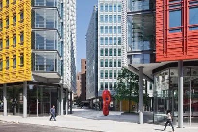 A group of people are walking down a sidewalk in front of a row of buildings