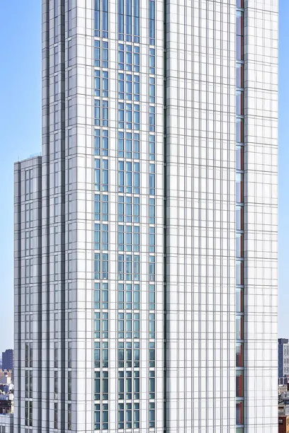 Aerial view of a modern high-rise building with a rooftop terrace, green space, and elevated train tracks in the background.