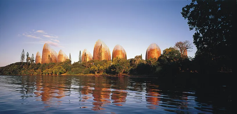 A large building is reflected in the water of a lake surrounded by trees