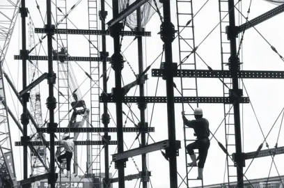 A black and white photo of a construction site with workers climbing scaffolding