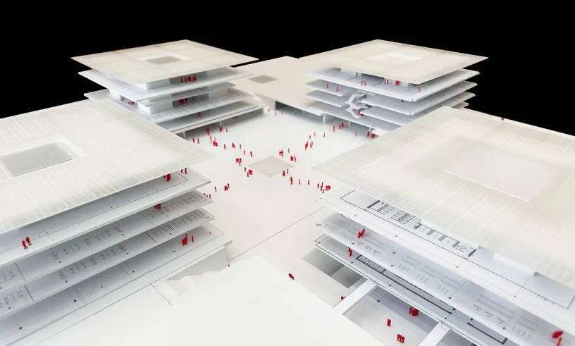 Architectural model of four white, multi-layered buildings arranged around a central plaza, populated by small red figures.