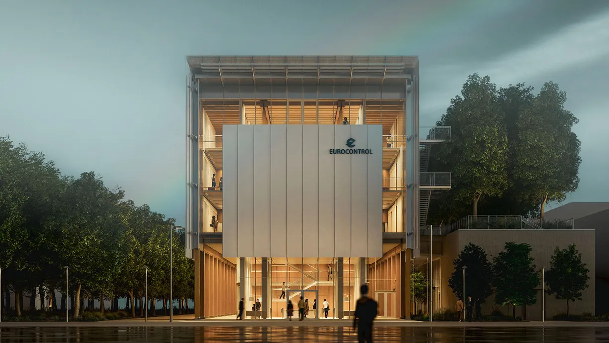 Exterior view of the modern Eurocontrol building with a glass facade and people inside, surrounded by trees.