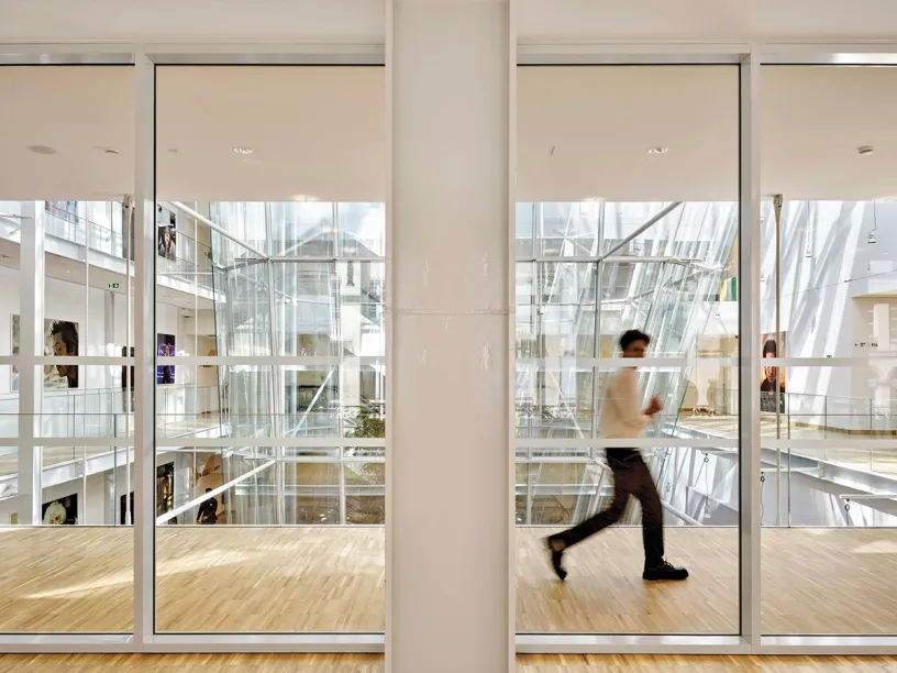 A man is walking through a building with a lot of windows