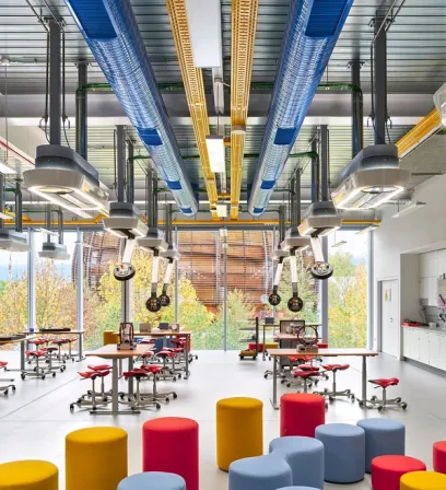 A large room with tables and stools and a lot of pipes hanging from the ceiling