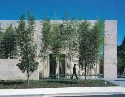 A man is walking in front of a building with trees in front of it