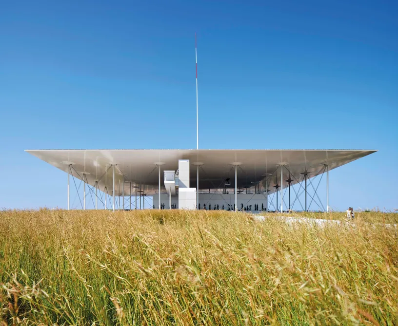 A large white building is sitting on top of a grassy hill