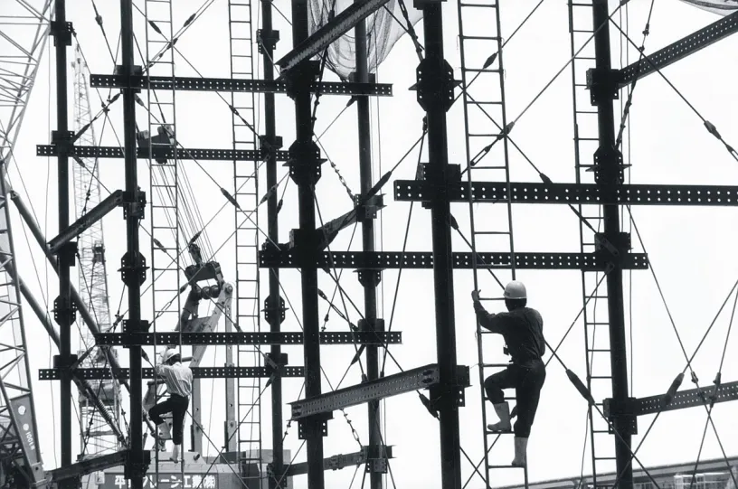 a black and white photo of a construction site with workers climbing ladders .