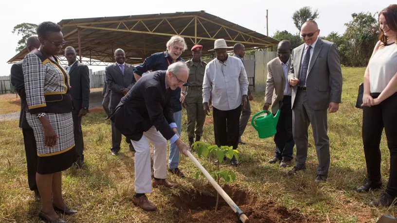 A group of people are standing around a man planting a tree