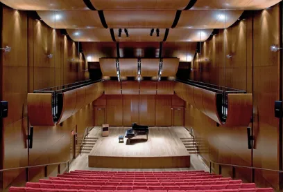 A large auditorium with a piano on the stage and red seats