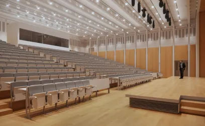A man is standing on a stage in an auditorium with rows of empty seats