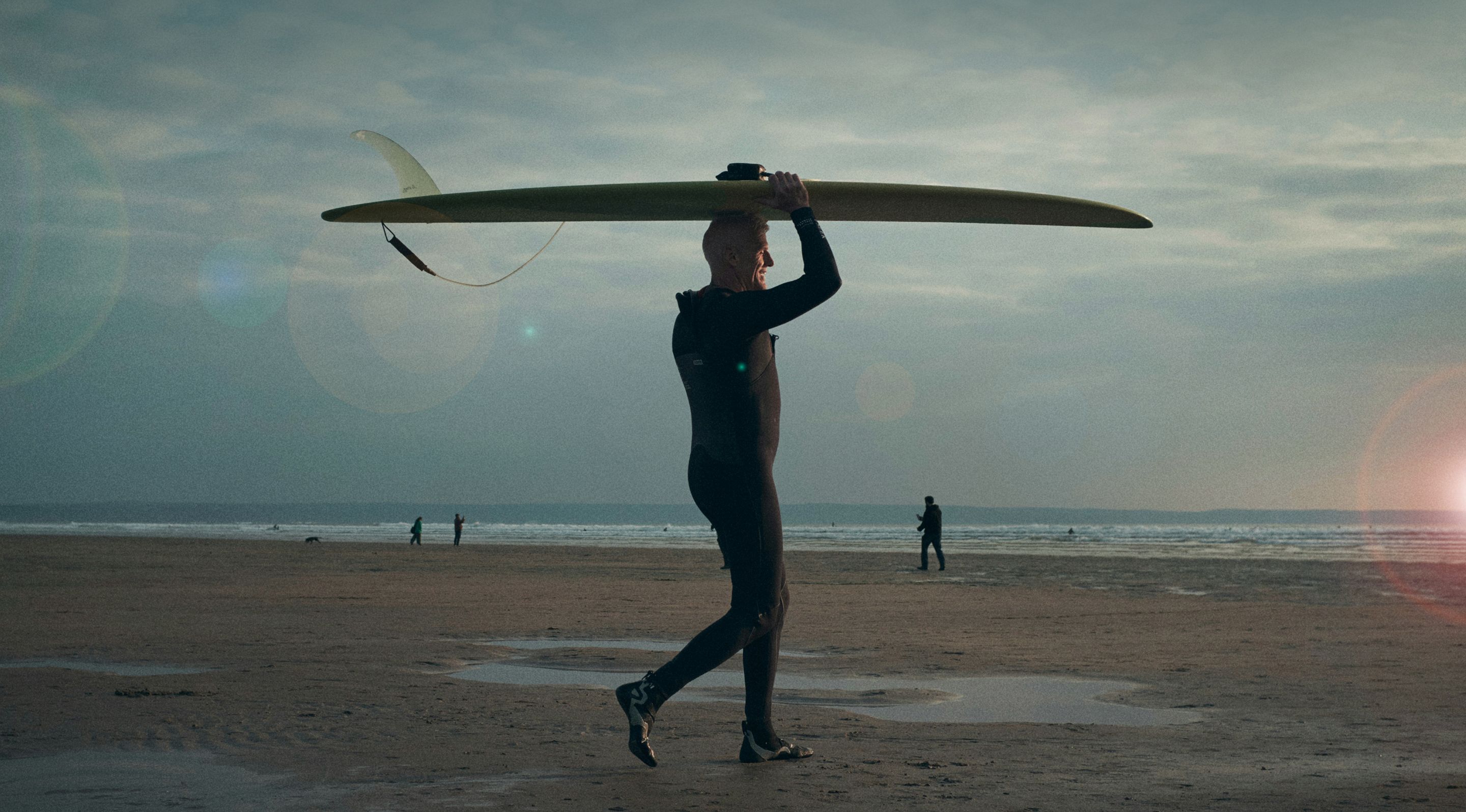 A man holding a surfboard above his head on a beach.