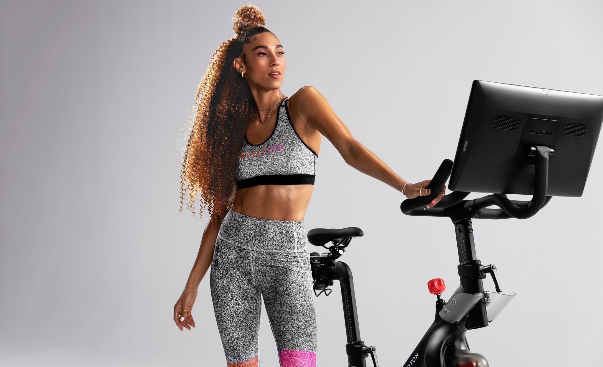 Woman in Peloton apparel posing next to bike