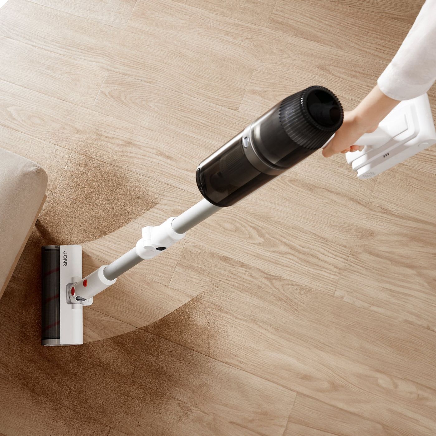 The handheld unit of the JONR VC08 Pro held in one hand and used along a wooden floor edge.