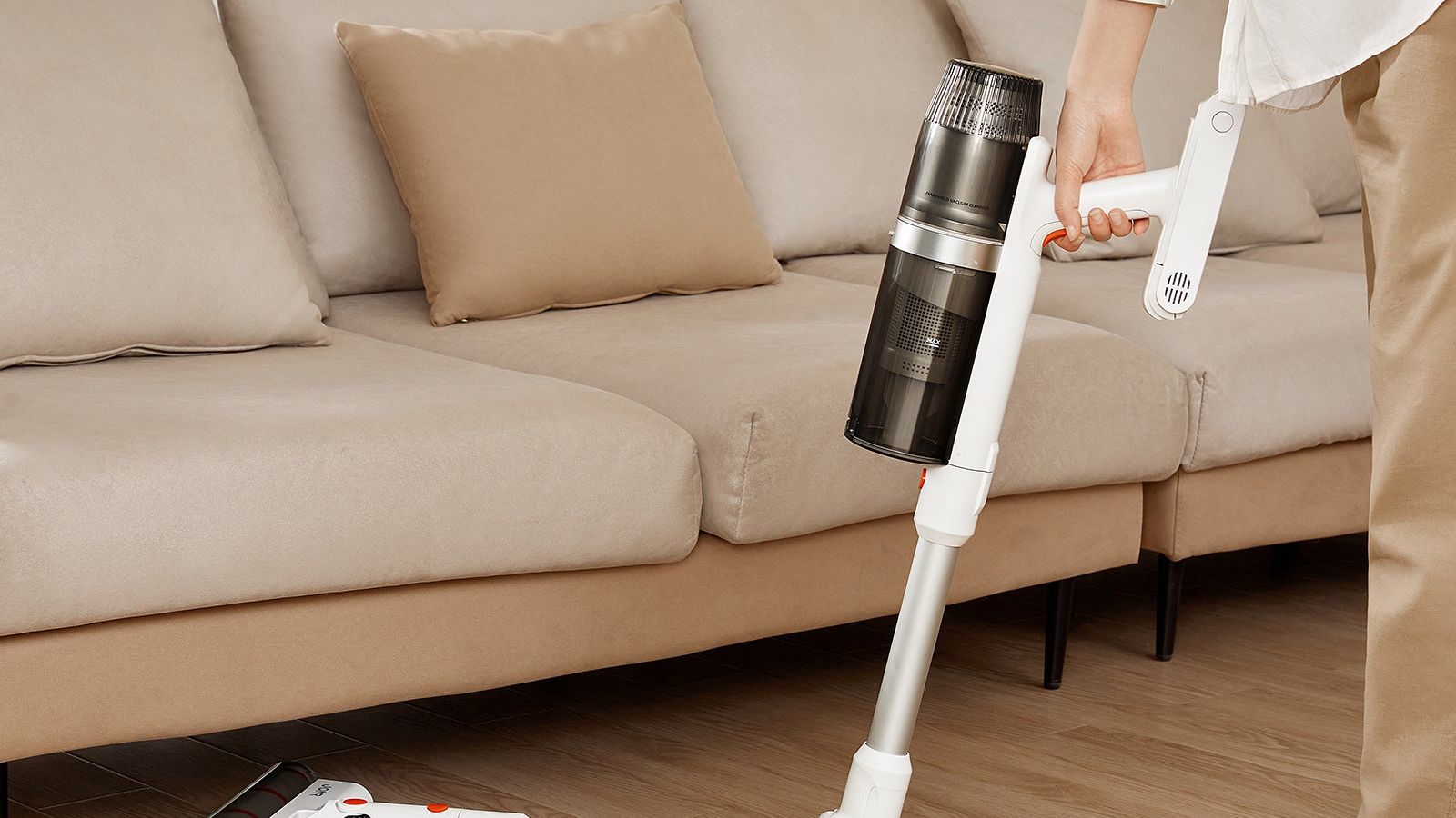 The JONR VC08 Pro cordless stick vacuum being used along the base of a sofa in a warm, tidy living room.