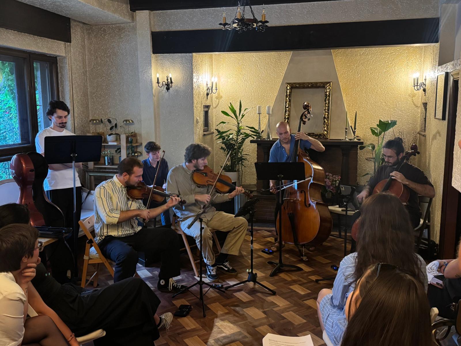 The quintet playing in a flower shop living room, double bass upright at the centre, listeners' heads in the foreground.