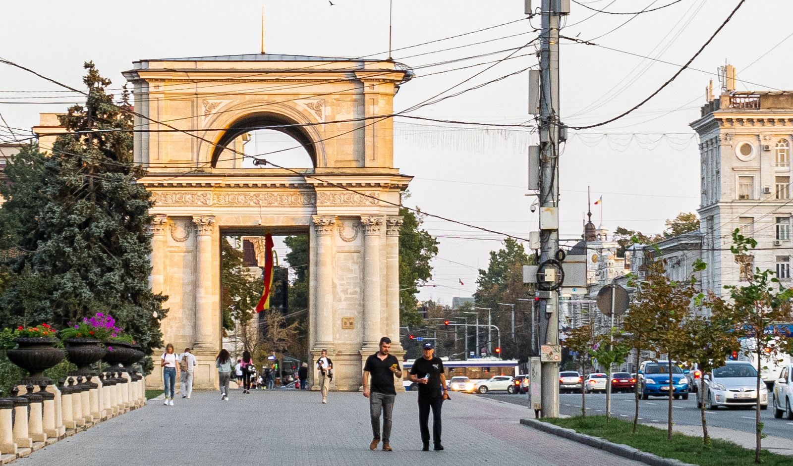 Several people walking down a wide street beneath a large white arch