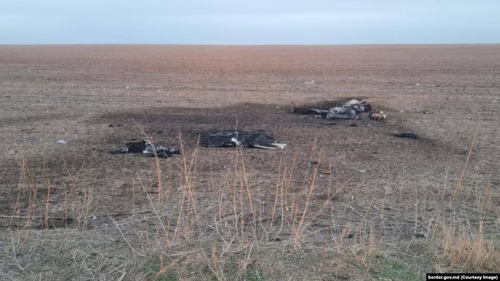 A crashed drone in a field with machine parts scattered over charred earth