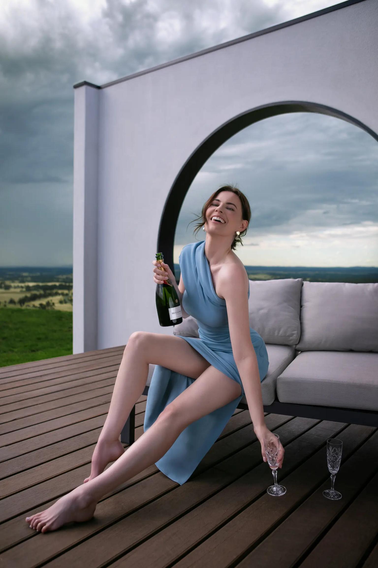 Woman in a blue robe seated on a deck beside an arched white wall