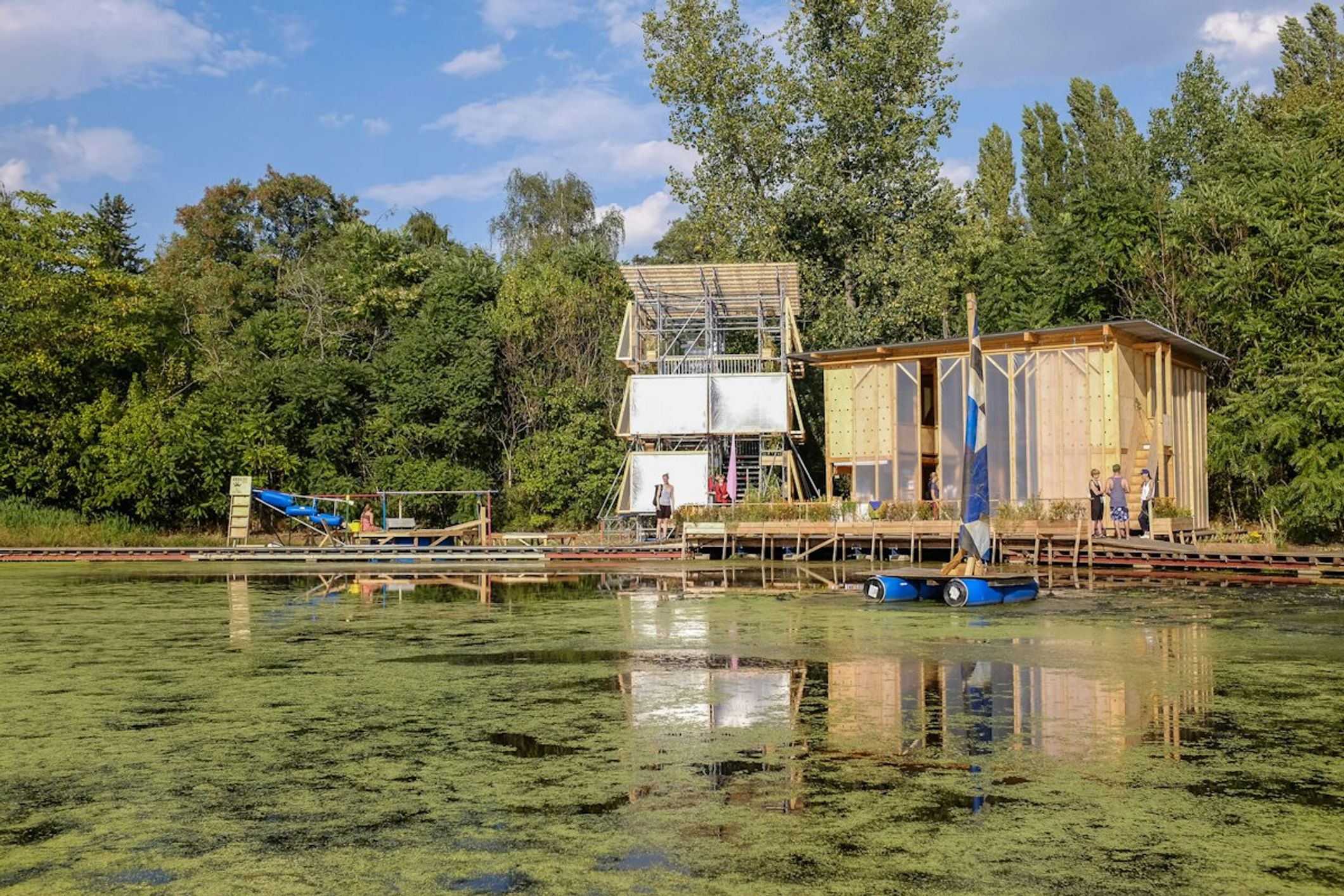 Timber boathouse on a pond covered in green duckweed, surrounded by trees