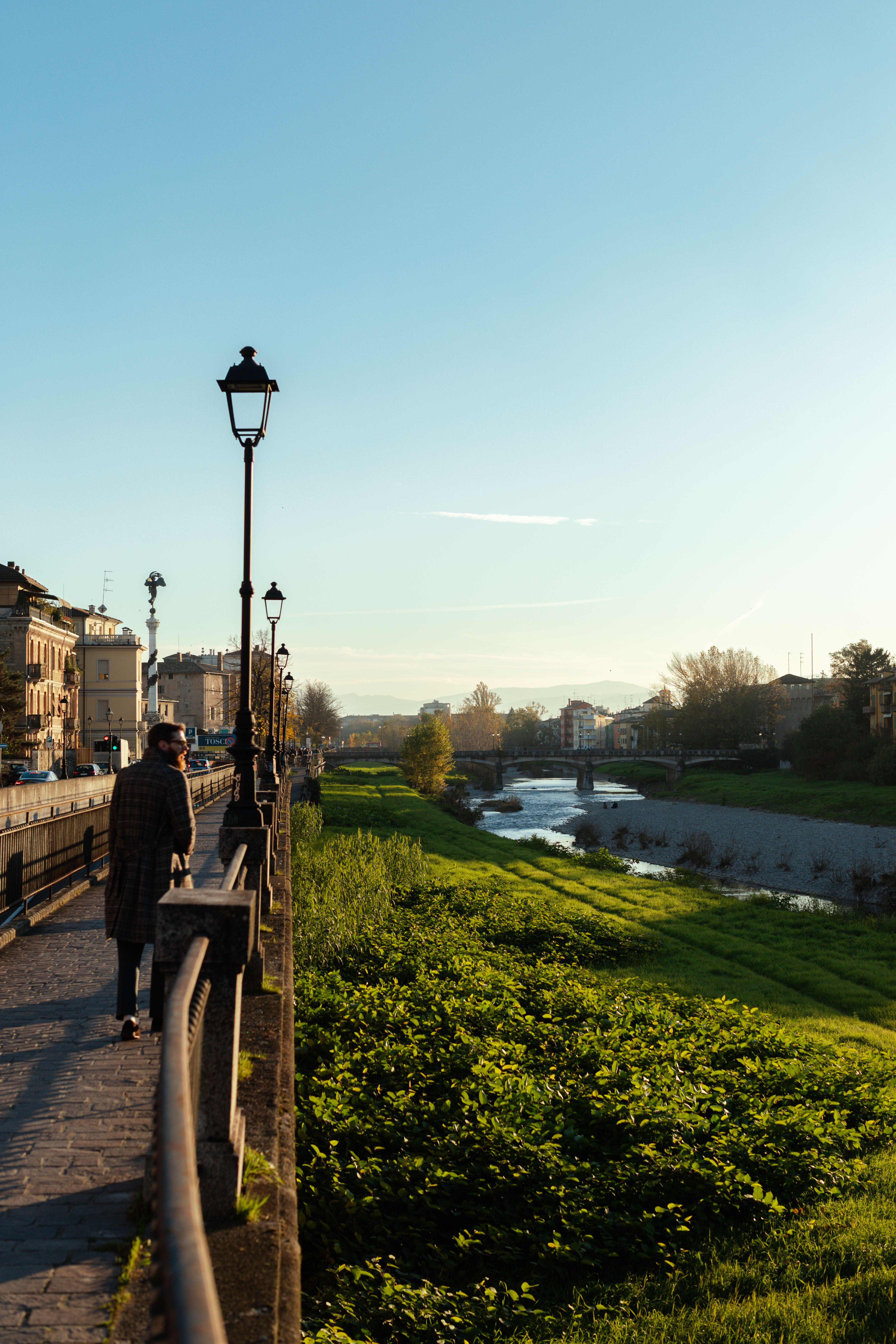 A tree-lined park path in Parma at dusk with a street lamp