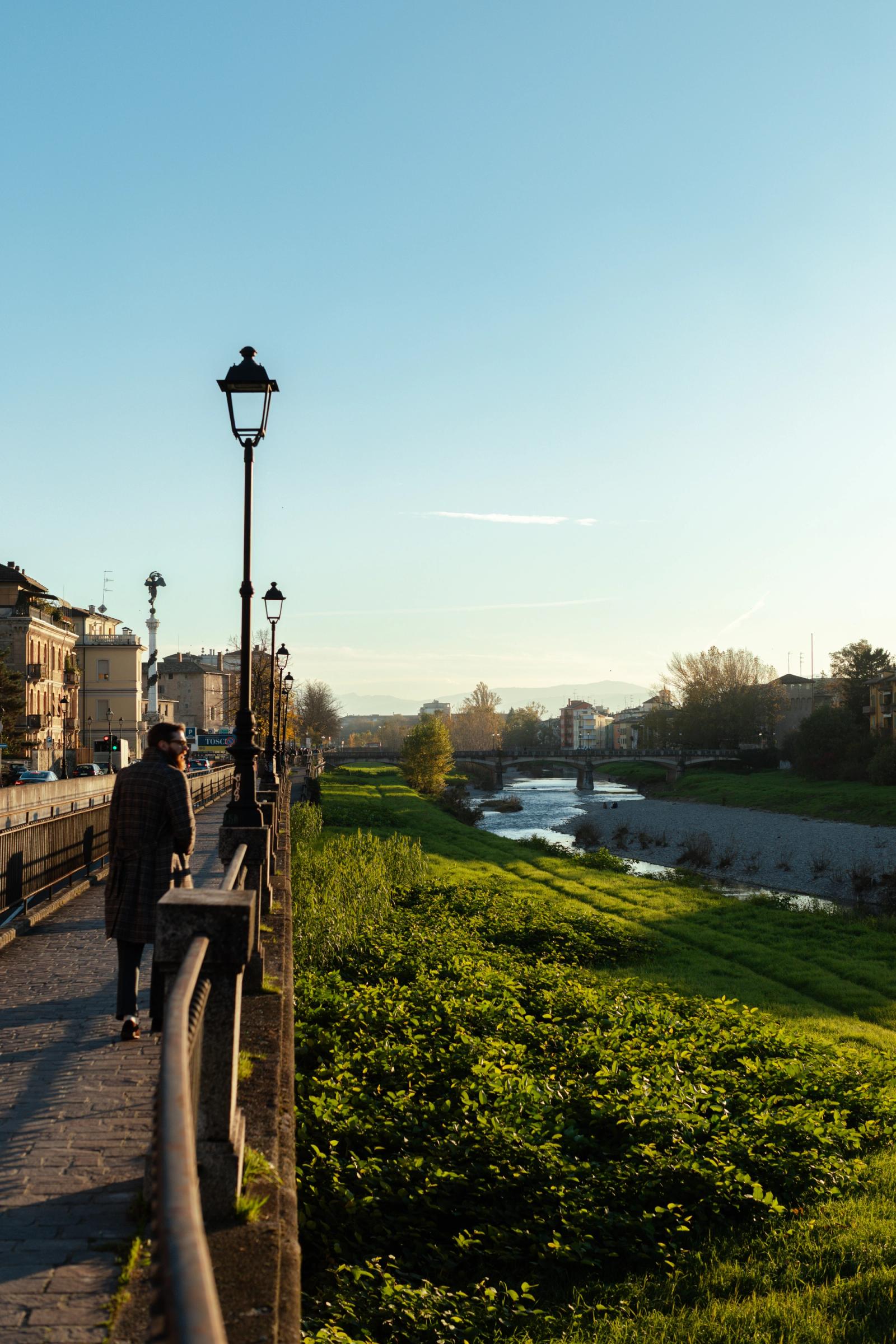 A tree-lined park path in Parma at dusk with a street lamp