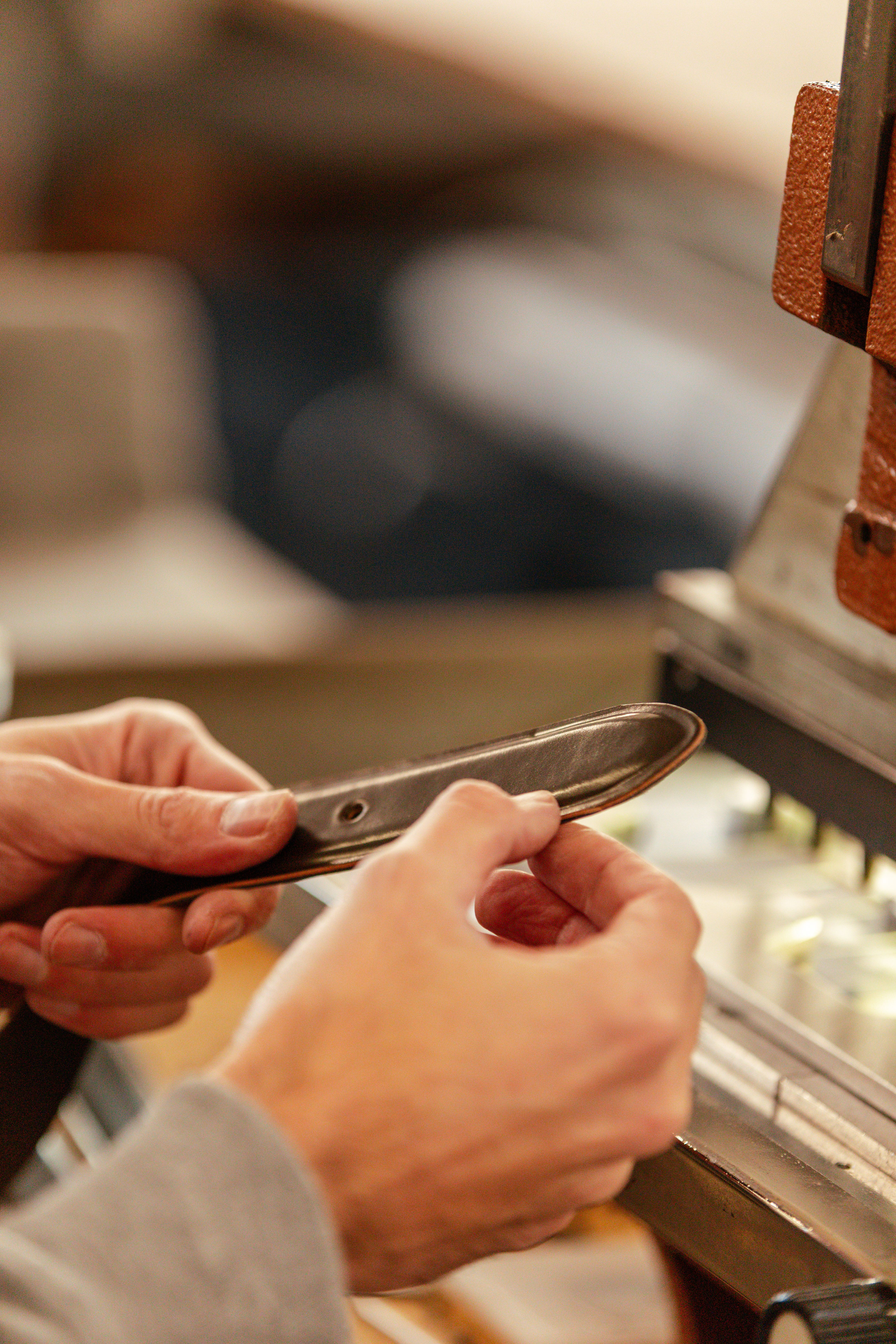 A craftsman's hands working a leather strap at a bench machine