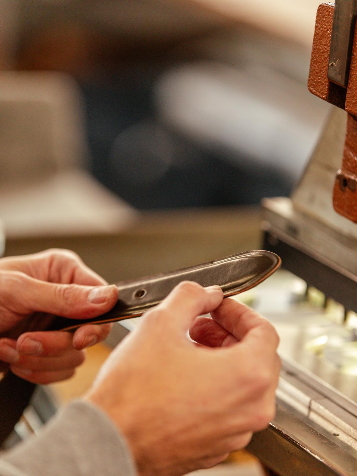 A craftsman's hands working a leather strap at a bench machine
