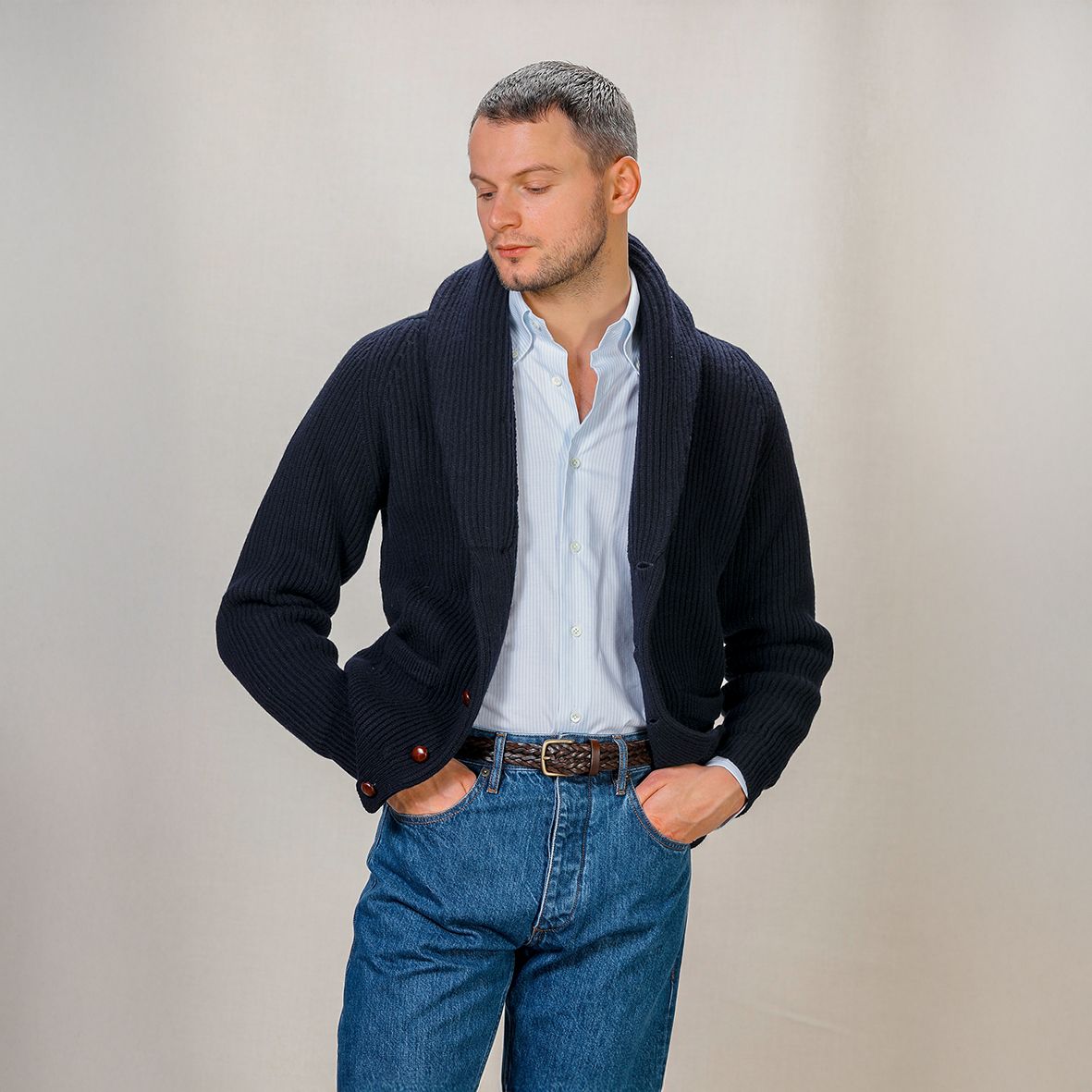A man in a navy shawl-collar cardigan, light blue shirt and jeans