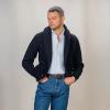 A man in a navy shawl-collar cardigan, light blue shirt and jeans