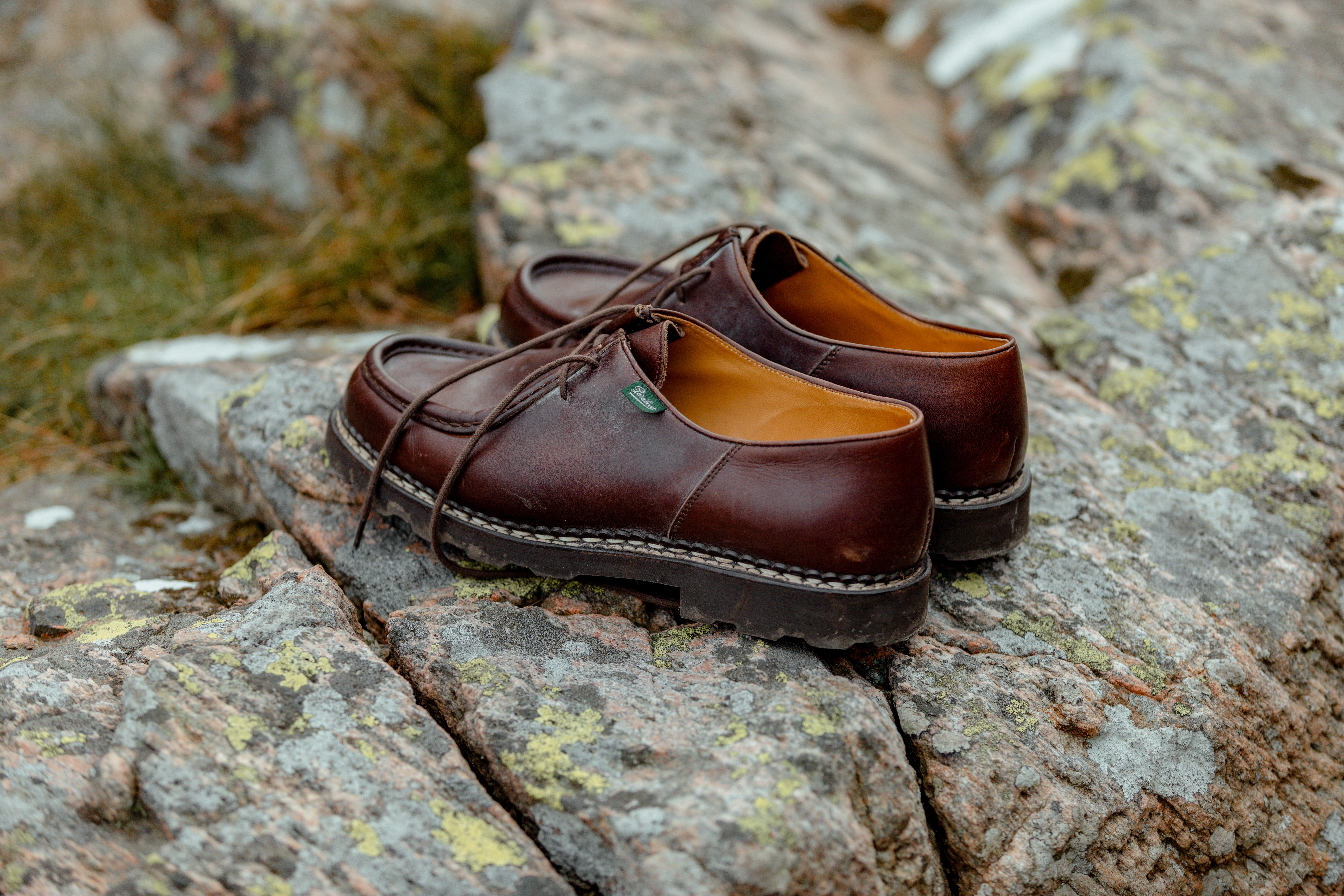 A pair of brown leather derby shoes resting on a moss-covered rock