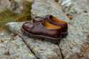 A pair of brown leather derby shoes resting on a moss-covered rock