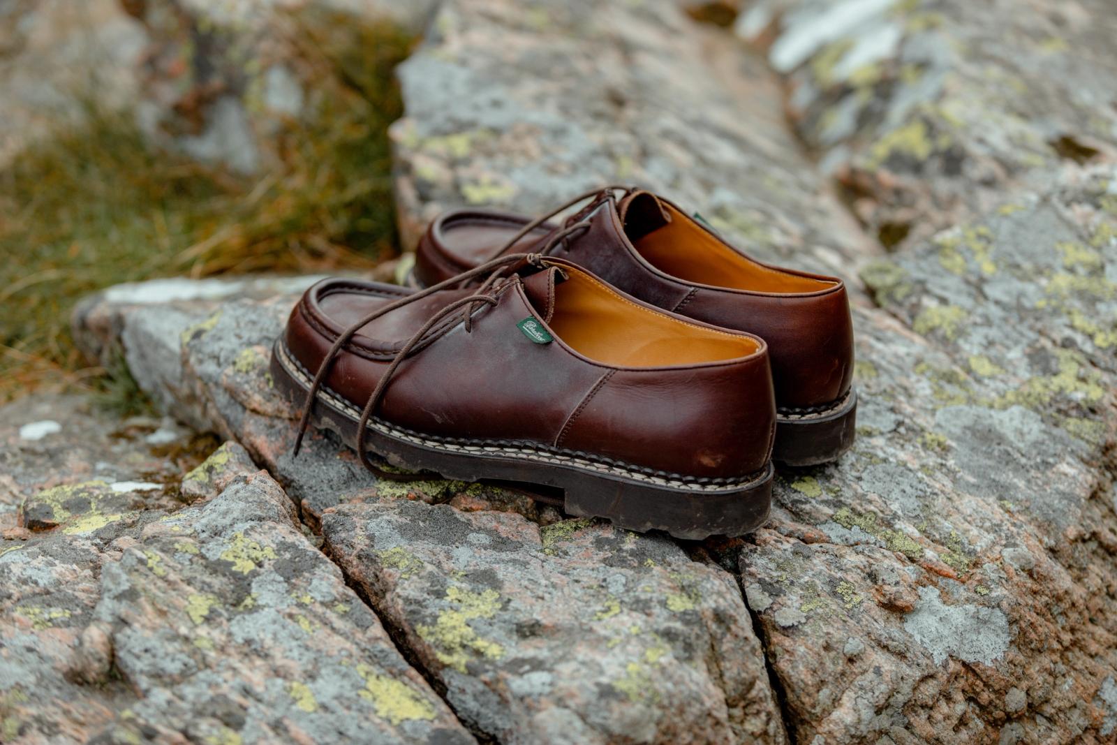 A pair of brown leather derby shoes resting on a moss-covered rock