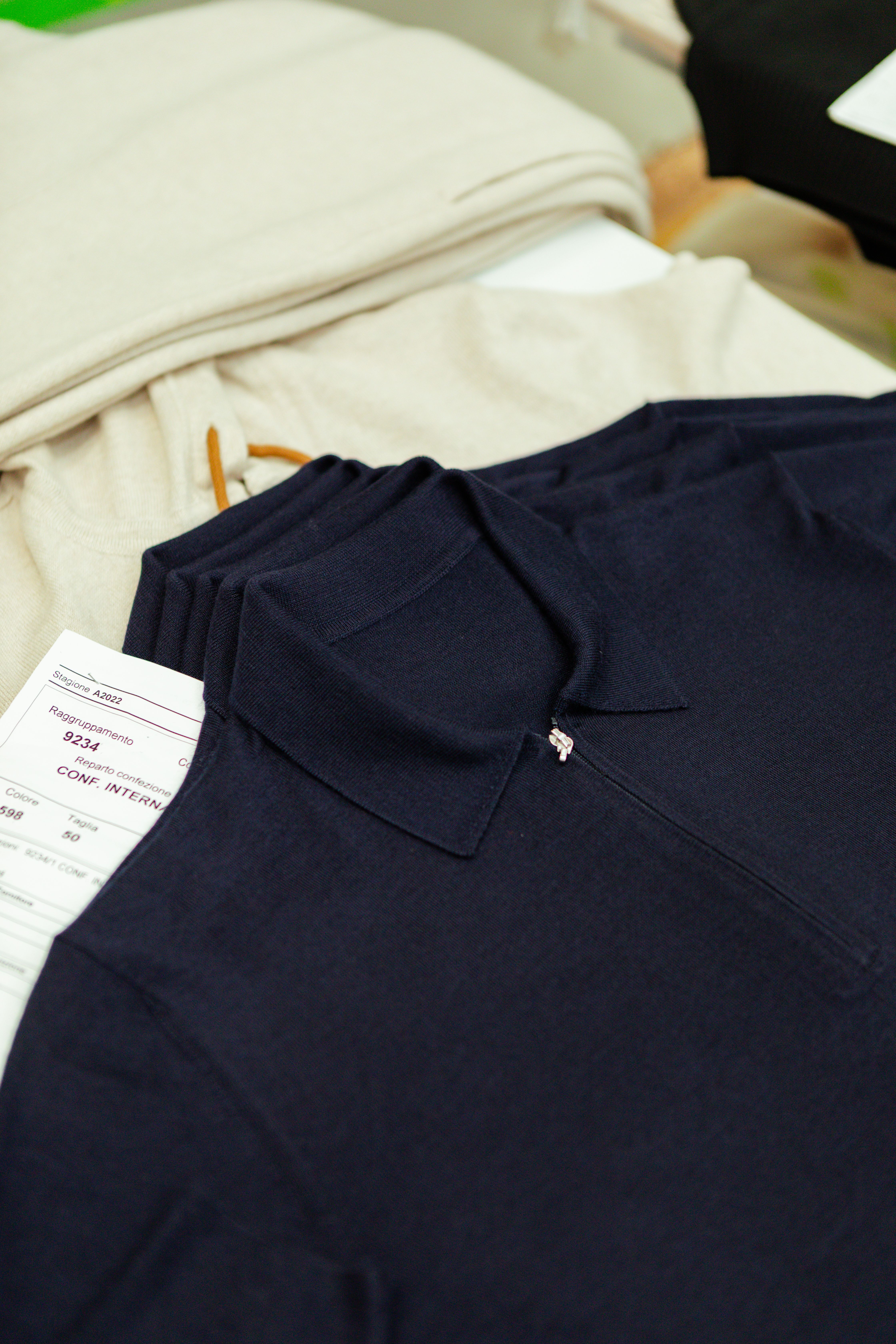 A folded navy knitted garment with a production tag resting on cream fabric