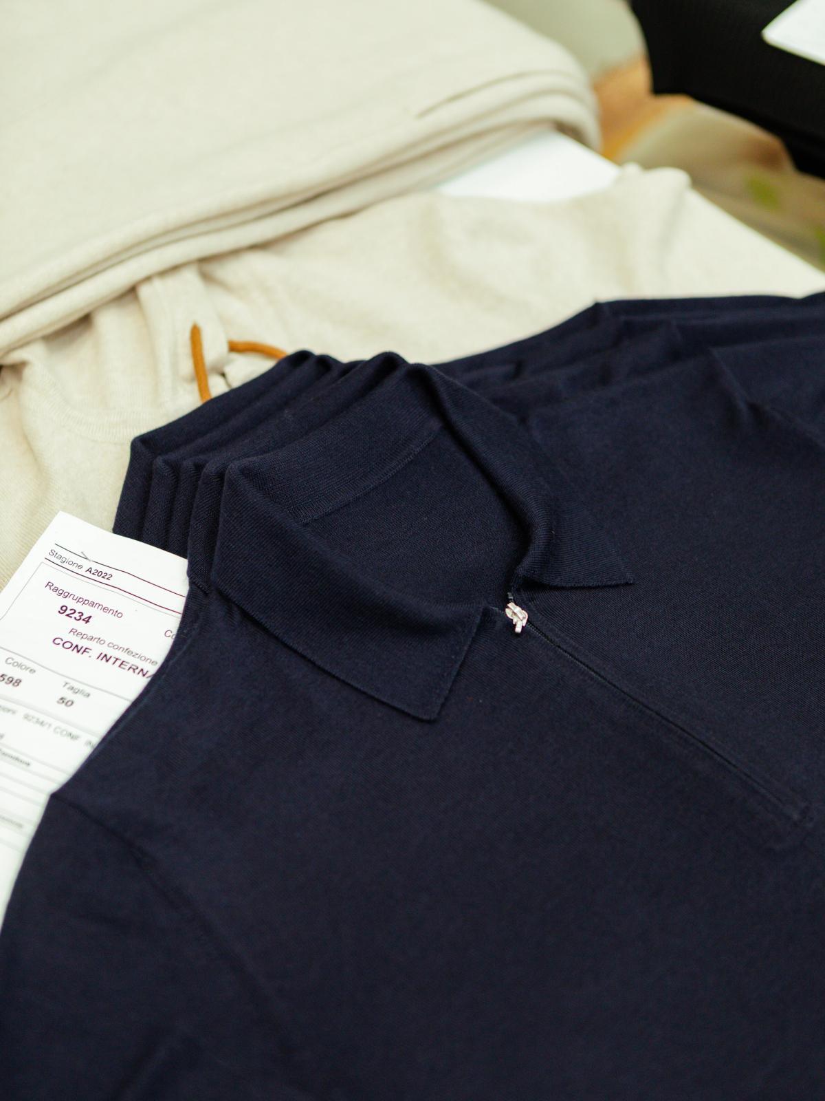 A folded navy knitted garment with a production tag resting on cream fabric